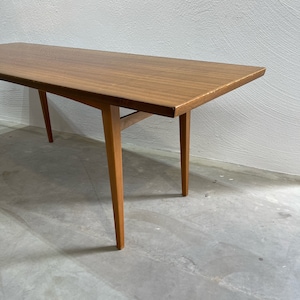 Könnte beinhalten: Ein moderner Couchtisch aus der Mitte des Jahrhunderts mit einer rechteckigen Holzplatte und vier schlanken Beinen. Der Tisch ist aus hellbraunem Holz gefertigt und hat ein schlichtes, elegantes Design.