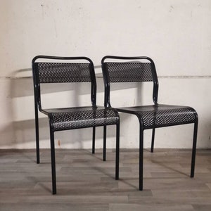 Könnte beinhalten: Zwei schwarze Metallstühle mit einem Netz-Sitz und Rückenlehne. Die Stühle stehen auf einem grauen Boden.