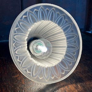 Peut inclure: Un abat-jour en verre transparent avec un bord festonné et un intérieur côtelé. L'abat-jour est éclairé par une ampoule.