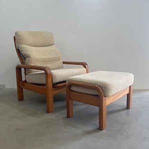 May include: A vintage armchair and footstool set. The chair features a high back with a cushioned headrest and armrests. The wooden frame and the cushions are a light beige colour. The footstool has a matching design.