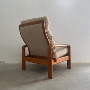 May include: A vintage armchair with a light brown fabric seat and back. The wooden frame has curved armrests and legs. The chair is a stylish piece of mid-century furniture, designed for comfort.