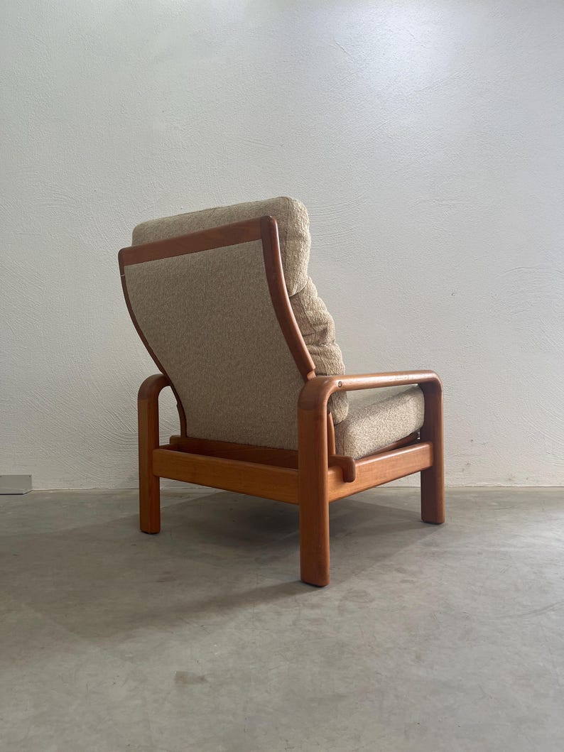 May include: A vintage armchair with a light brown fabric seat and back. The wooden frame has curved armrests and legs. The chair is a stylish piece of mid-century furniture, designed for comfort.