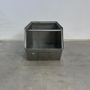 Può includere: Un contenitore in metallo color argento con apertura frontale, una barra di supporto orizzontale sulla parte superiore e un porta etichette rettangolare sul pannello frontale. Il contenitore presenta un piccolo adesivo circolare verde.