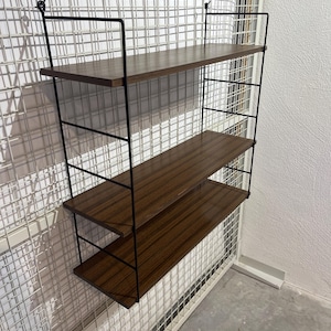 Könnte beinhalten: Ein dreistufiges Wandregal. Die Regale sind aus dunklem Holz mit sichtbarer Maserung gefertigt. Der Rahmen ist aus schwarzem Metall und das Regal wird an Haken aufgehängt. Die Regale sind ca. 76 cm breit.