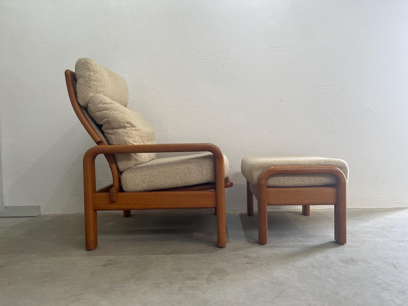 May include: A vintage lounge chair and footstool set. The chair features a wooden frame with a curved back and armrests. The cushions are upholstered in a light beige fabric. The footstool has a matching wooden frame and upholstered top.