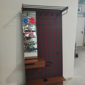 Könnte beinhalten: Ein Holz-Kleiderständer mit Spiegel und kariertem Design. Der Ständer hat ein Regal, einen Kleiderhaken und einen Hutständer.