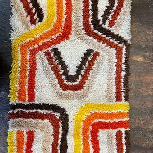 Peut inclure: Tapis rectangulaire texturé avec un fond crème et un design rétro. Le motif présente des lignes et des formes courbes marron, orange et jaune. Le tapis a une texture touffue et bouclée.