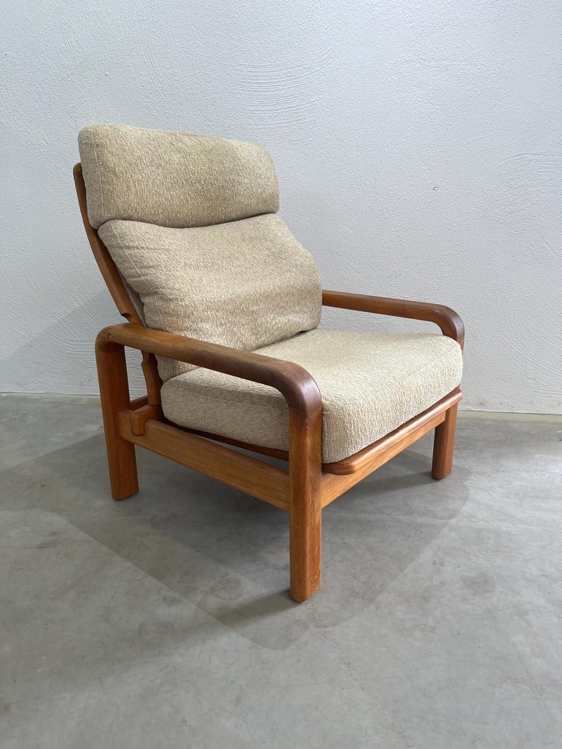 May include: A vintage armchair featuring a light beige fabric seat and backrest. The wooden frame has a warm, natural finish. The chair has a high back and armrests, offering a comfortable seating experience. The chair's dimensions are approximately 80 cm in height.