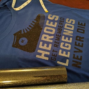 May include: A blue t-shirt with a black glitter design of a boot and the text "HEROES GET REMEMBERED LEGENDS NEVER DIE".