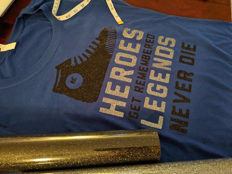 May include: A blue t-shirt with a black glitter design of a boot and the text "HEROES GET REMEMBERED LEGENDS NEVER DIE".