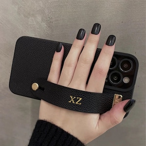 Puede incluir: Funda de teléfono de cuero negro con una correa de cuero negro y letras doradas que dicen "XZ".