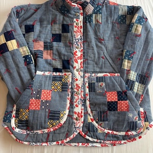 May include: A quilted jacket in shades of blue with patchwork squares in red, yellow, and navy. The jacket has a round collar and two front pockets. The edges are trimmed with a red and white floral pattern.