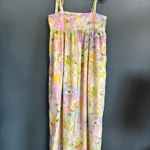 May include: A long, floral print dress with tie straps, hanging on a white hanger. The dress features a pattern of pink, yellow, and purple flowers on a white background. The straps are tied at the shoulders.