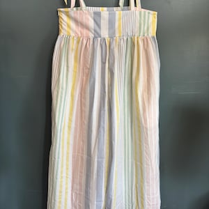 May include: A pastel striped jumpsuit with tie straps, hanging on a white hanger. The jumpsuit features vertical stripes in shades of pink, yellow, blue, and green. The fabric appears lightweight and suitable for warm weather.