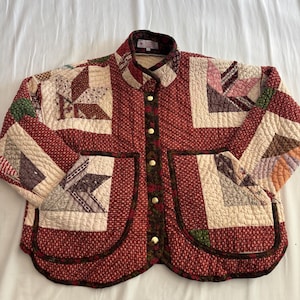 May include: A quilted jacket featuring a patchwork design with various red, cream, and brown floral and geometric patterns. The jacket has a stand-up collar, long sleeves, two large front patch pockets, and a front closure with five gold-tone metal buttons.