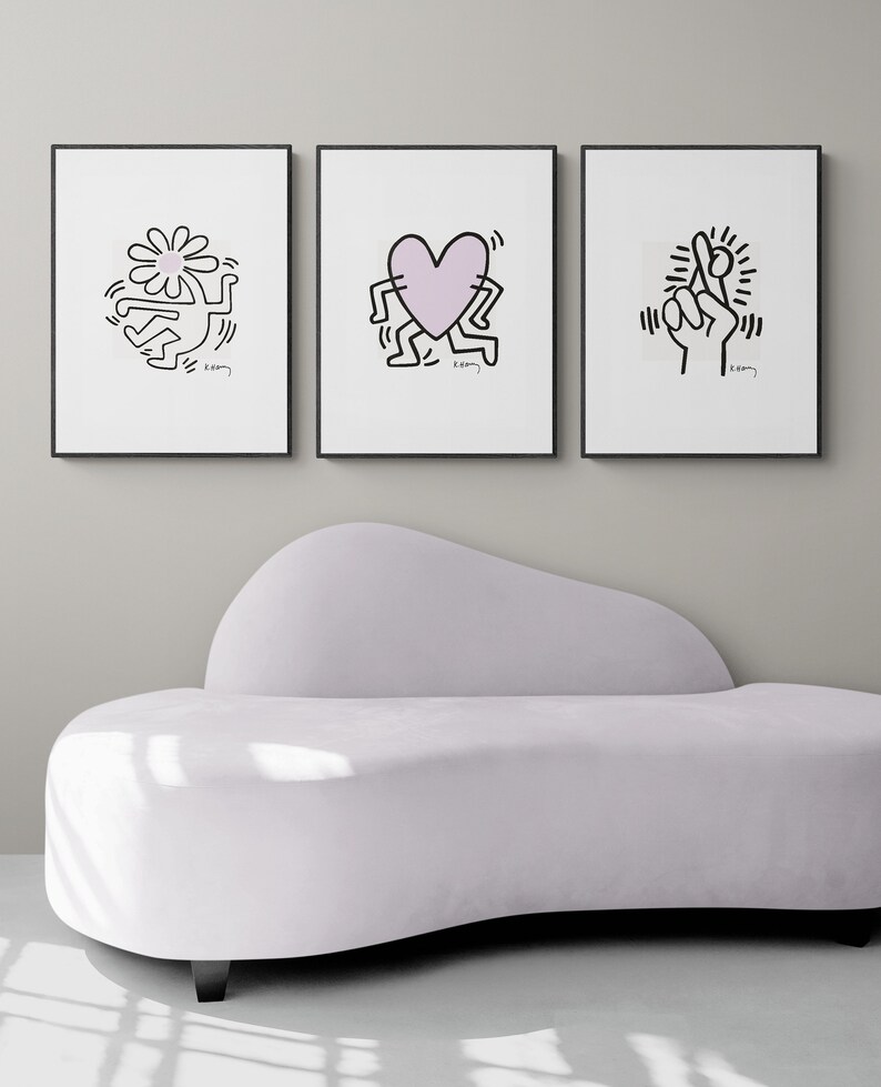 May include: Three black framed prints with white backgrounds and black line drawings of a person holding a flower, a person holding a heart, and a person holding up two fingers. The prints are hanging on a white wall above a white couch.