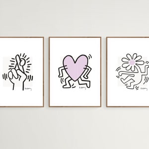 May include: Three framed prints of black and white line drawings by artist Keith Haring. The first print features a hand with crossed fingers, the second print features a heart-shaped figure with legs, and the third print features a figure with a daisy for a head.