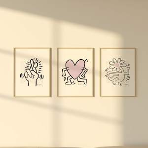 May include: Three framed black and white illustrations with pink accents. The illustrations are of a hand making a pinky promise, a heart with legs, and a figure with a flower on its head. Each illustration is signed "K. Haring".