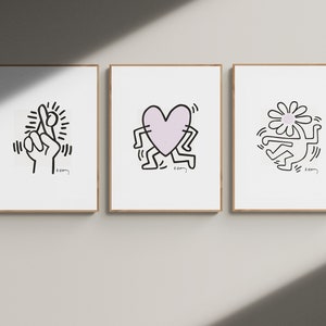 May include: Three framed prints with black and white line drawings by Keith Haring. The first print features a hand with crossed fingers, the second print features a heart with legs, and the third print features a flower with a person inside.