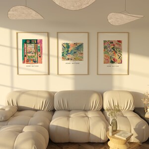 May include: Three framed art prints of colorful landscape paintings by Henri Matisse. The prints are hung on a white wall above a beige sofa.