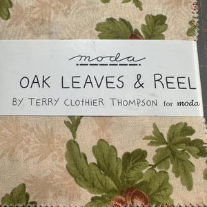 May include: Fabric squares with a floral pattern featuring green oak leaves and beige and pink flowers. The text "OAK LEAVES & REEL" is printed on a white label, along with the brand "moda" and the designer's name.