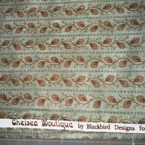 Peut inclure: Tissu à motifs répétés de feuilles et de vignes marron sur fond vert clair. Des rayures pointillées séparent les vignes. Le texte "Chelsea Boutique by Blackbird Designs" est imprimé sur un ruban blanc. Idéal pour les projets créatifs.