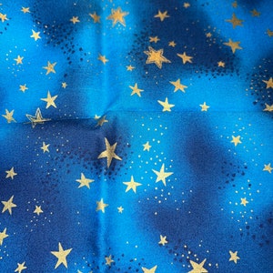 Może przedstawiać: Zbliżenie tkaniny z niebiańskim wzorem. Tło to gradient od głębokiego niebieskiego do jaśniejszego niebieskiego, przypominający nocne niebo. Złote gwiazdy o różnych rozmiarach są rozrzucone po tkaninie, a mniejsze kropki dodają efektu gwiezdnego. Tkanina ma lekki połysk.