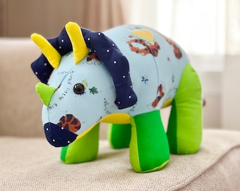 May include: A blue and green plush toy shaped like a triceratops. The toy has yellow horns and a black and white polka dot pattern on its head.