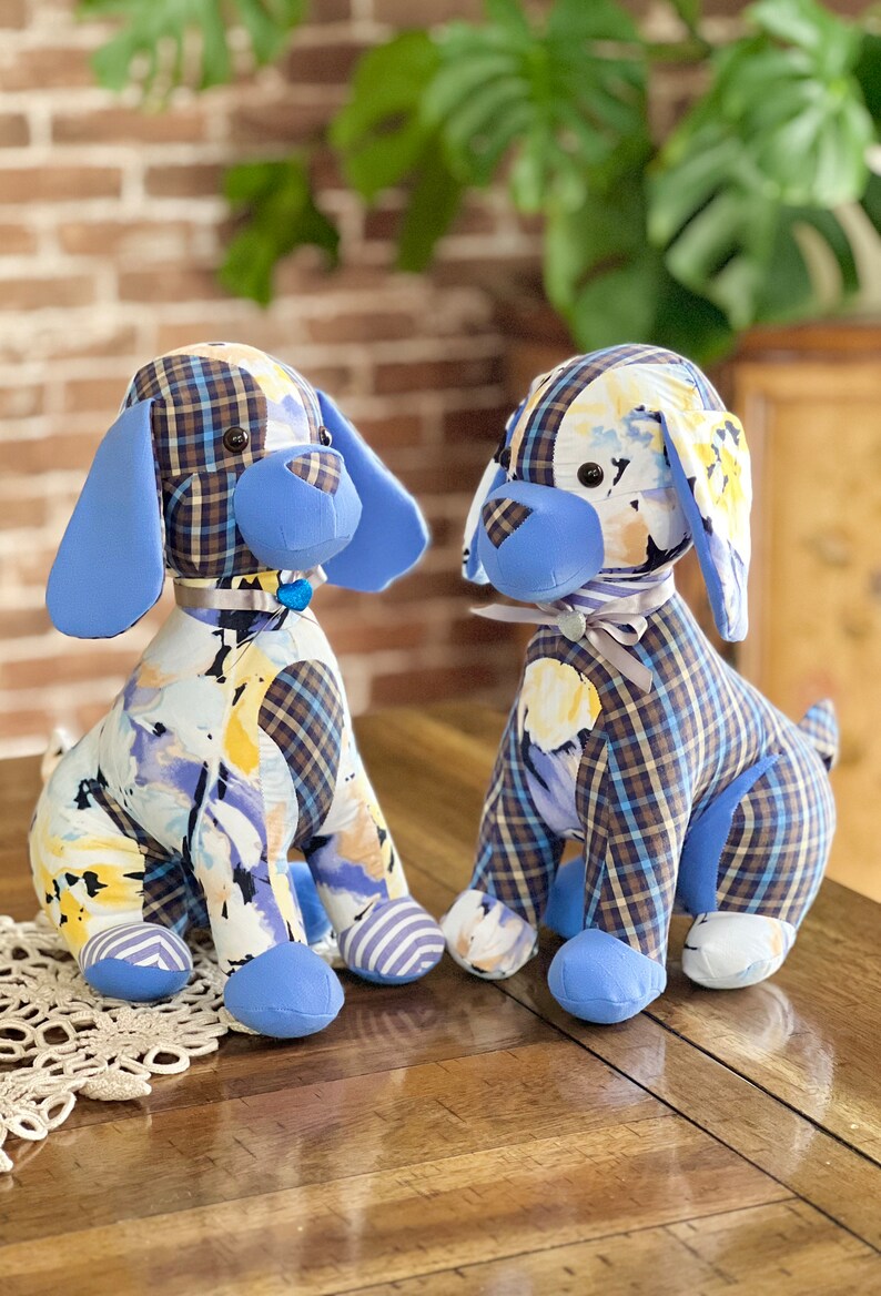 May include: Two blue and white patchwork fabric dog plushies with black eyes and blue noses. The plushies are sitting on a wooden table.