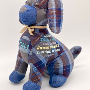 May include: A blue and gray plaid dog-shaped stuffed animal with a tan bow. The dog has a brown button eye and the text "This is a shirt I used to wear Whenever you hold it Know that I am there" is embroidered on the dog's chest. The dog's name "Poppy" is embroidered on the left side of the dog.