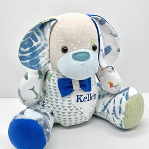 May include: A plush dog toy with a light tan head and ears, patterned with white stars and blue tie-dye. The dog has a blue bow tie and a heart-shaped patch embroidered with the name "Keller". The dog's body is patterned with blue and green shapes.