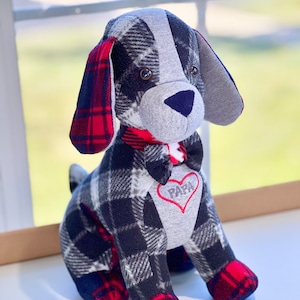 May include: A plush dog toy with a black and white plaid pattern, red and black plaid ears, and a gray face. The dog is wearing a red bow tie and has a red heart with the word "PAPA" embroidered on its chest.