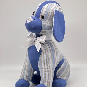 May include: A blue and white striped plush dog toy with a white bow. The dog is sitting with its legs crossed and has brown eyes.
