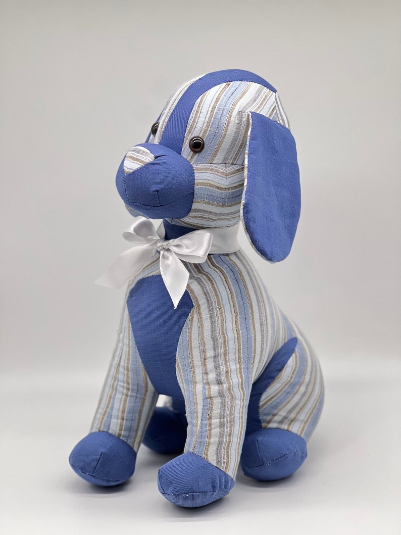 May include: A blue and white striped plush dog toy with a white bow. The dog is sitting with its legs crossed and has brown eyes.