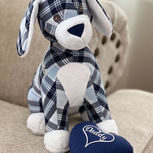 May include: A blue and white plaid stuffed dog toy with a white heart-shaped pillow that says "Daddy" in white embroidery. The dog is sitting on a beige couch.