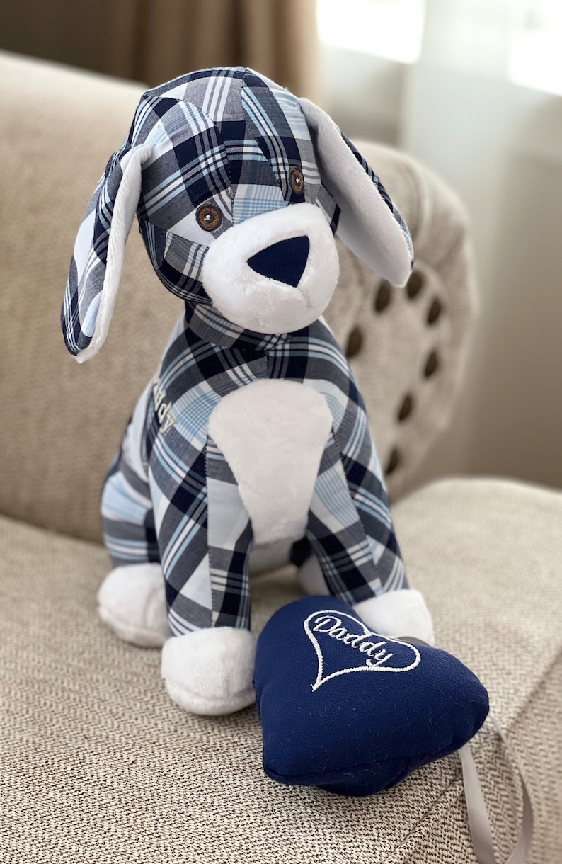 May include: A blue and white plaid stuffed dog toy with a white heart-shaped pillow that says "Daddy" in white embroidery. The dog is sitting on a beige couch.