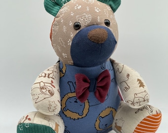 May include: A patchwork teddy bear with a blue and white lion print body, green ears, and a burgundy bow tie. The bear is sitting on a white surface.