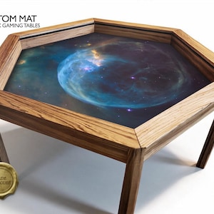 Op de afbeelding: Een zeshoekige houten speeltafel met een aangepaste mat met een diepe ruimte nevelprint. De tafel heeft een lichtbruin houten frame en een verzonken midden. Tekst linksboven leest CUSTOM MAT FOR HEX GAMING TABLES.