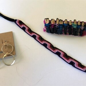 May include: A set of three handmade jewelry items: a black and pink woven bracelet, a pair of gold hoop earrings, and a colorful woven doll figurine keychain.