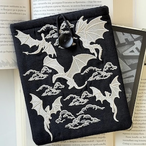 May include: Black e-reader case with a white embroidered design of dragons and clouds. The case has a drawstring closure and a button.
