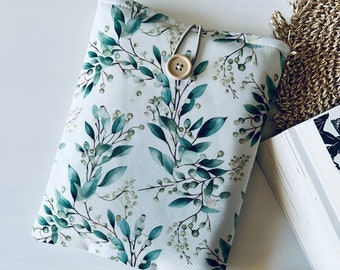 May include: A white book cover with a green leafy pattern and a wooden button closure. The cover is lying on a white surface.