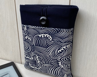 Könnte beinhalten: E-Reader-Hülle mit einem marineblauen und weißen Wellenmuster. Der obere Teil ist einfarbig marineblau mit Knopfverschluss. Im Hintergrund ist ein E-Reader zu sehen.