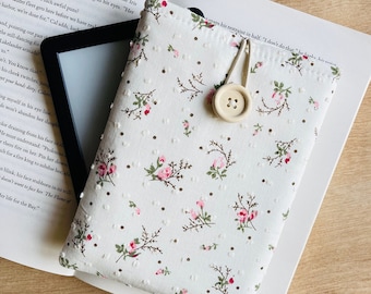 May include: A white and pink floral patterned e-reader cover with a white button and a brown strap.