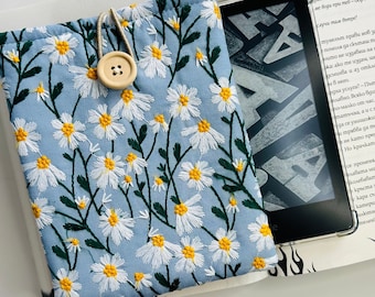 May include: A light blue fabric e-reader case with a white daisy pattern. The case has a button closure and a drawstring.