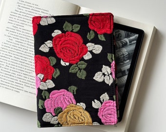 May include: A black fabric e-reader cover with embroidered red, pink, and yellow roses. The cover is designed to fit a Kindle or other e-reader.