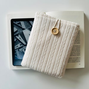 Peut inclure: Une housse pour liseuse en tricot blanc avec une fermeture à bouton. La housse est faite d'un tissu doux et texturé et a un design simple et élégant.