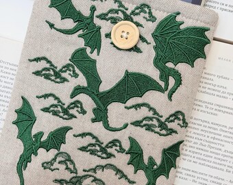 Op de afbeelding: Beige stoffen e-reader hoes met groene geborduurde draken en wolken. Voorzien van een houten knoopsluiting. De hoes is ontworpen voor een e-reader.