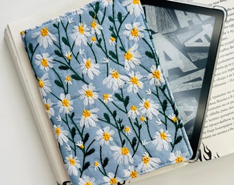May include: A light blue book cover with a white daisy floral pattern. The cover is made of fabric and has a soft, textured feel.