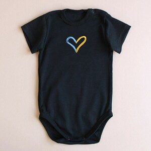May include: A black short-sleeved bodysuit with a yellow and blue heart embroidered on the front.