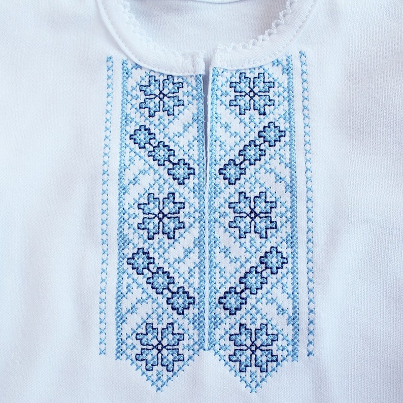 Puede incluir: Camisa blanca bordada con un patr&oacute;n floral azul y blanco. El bordado es de estilo ucraniano tradicional.